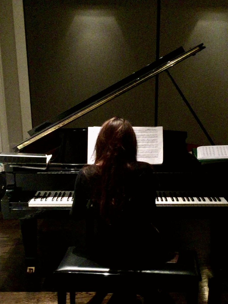 Courtney seated at a grand piano from behind in soft light